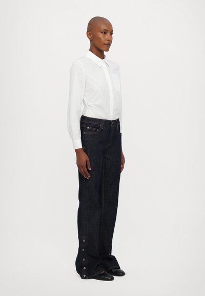 Hvit skjorte med knapper og brystlomme, kombinert med mørkeblå denimjeans med sidestittere og løs passform. Svarte sko fullfører antrekket.