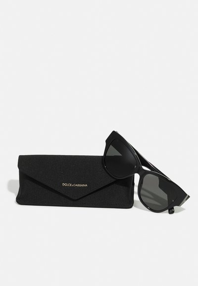 Černé sluneční brýle s ostrým kočičím designem, umístěné vedle černého texturovaného pouzdra se zlatým logem "DOLCE & GABBANA".