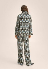 Conjunto en blanco y negro con estampado de formas geométricas; acentos azules en una camisa de corte relajado y pantalones de pierna ancha. Tejido suave con una textura lisa.