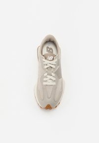 Zapatilla deportiva gris claro con parte superior de ante, puntera redondeada y cordones blancos. Presenta una suela de goma y un logo sutil en el lateral.