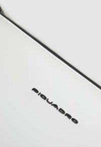 Borsa in pelle bianca con bordature nere e logo "Piquadro" in rilievo. Texture liscia con cuciture a contrasto, caratterizzata da un design minimalista.