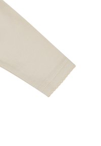 Beige fabric sleeve with a scalloped hem, featuring smooth texture and subtle stitching. Part of a garment design.