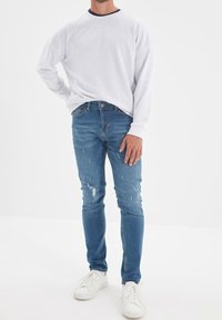 Chemise blanche à manches longues avec un col bleu marine, associée à un jean slim bleu usé et des baskets blanches. Design simple, look décontracté.