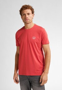 T-shirt in cotone rosso con collo rotondo, maniche corte e stampa grafica circolare sul lato sinistro del petto. Tessuto morbido, vestibilità rilassata.