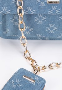 Denim-Umhängetasche mit goldenem Kettenriemen, ausgestattet mit einem Reißverschlussfach. Hellblauer Stoff zeigt ein dezentes weißes Muster und ein Logo-Tag.