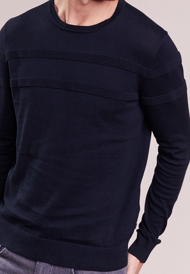 Homme portant un pull noir à manches longues avec des rayures horizontales côtelées sur la poitrine et le haut des bras.