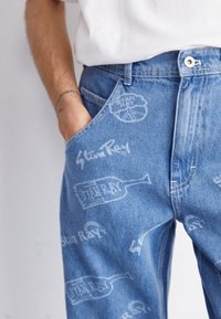 Hellblaue Denim-Jeans mit weißen Markenmotiven und Flaschen-Designs. Standardpassform mit Fronttaschen und einem Knopfverschluss.