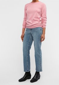 Rosa stickad tröja, rundad hals, långa ärmar. Ljusblå raka jeans, medium hög midja. Svarta ankelstövlar med kraftig klack.