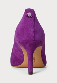 Lila nubukka korkokenkä, jossa on terävä kärki ja hoikka stiletto-korko. Takana hopea logo-yksityiskohta. Sileä pinta.