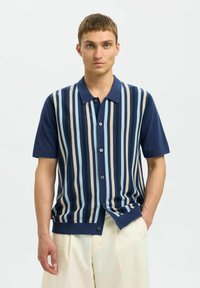 Majica s kratkimi rokavi v mornarsko modri in smetanasti črtasti zasnovi z gumbnim zapenjanjem in mehkimi pletenimi vlakni. Ima klasičen ovratnik in podrobnosti ob stranskih šivih.