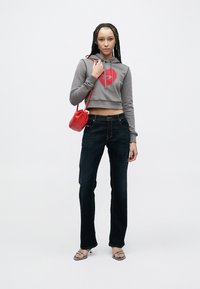 Sivá skrátená mikina s červeným srdcovým motívom, v kombinácii s tmavomodrými džínsami so širokými nohavicami. Modelka drží malú červenú kabelku a nosí metalické sandále na podpätku.