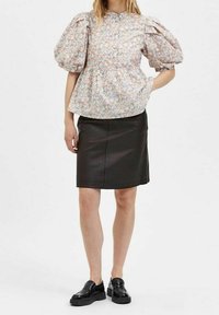 Blusa floreale con maniche a sbuffo e vita aderente, abbinata a una gonna in pelle nera fino al ginocchio e scarpe nere con lacci.