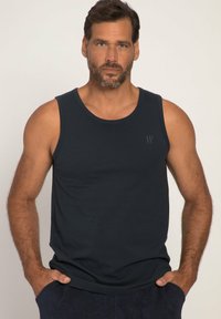 Tmavě modrý tílko vyrobené z hladkého bavlněného materiálu, s kulatým výstřihem a bez rukávů. Diskrétní logo na hrudi dodává detail.