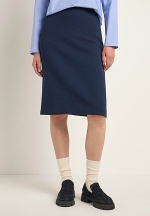 Marineblauer Ripp-Rock in dehnbaren Material, kniefrei mit einem seitlichen Schlitz, kombiniert mit cremefarbenen Socken und dunklen Mokassins.