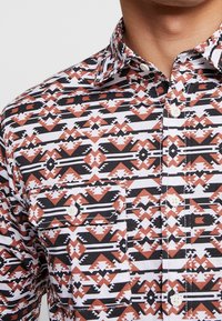 Katoenen shirt met korte mouwen en een geometrisch patroon in roest, zwart en wit. Voorzien van een button-down kraag en een borstzak.