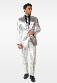 Silver metallic suit with a shiny finish, featuring a one-button blazer and slim-fit trousers, paired with a black shirt and tie.