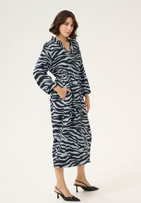 Accappatoio con stampa zebra in nero e grigio chiaro, caratterizzato da maniche lunghe, vita con cintura e tasche laterali. Tessuto morbido con vestibilità comoda.