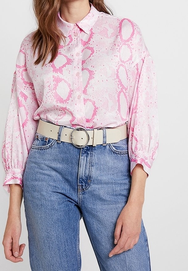 Chemise rose clair à boutons avec motif serpent, associée à un jean en denim bleu taille haute et une large ceinture crème avec une boucle circulaire.