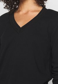 Czarna bluzka z długim rękawem i dekoltem w serek, z teksturowanym kołnierzem, wykonana z gładkiej tkaniny o luźnym kroju. Minimalistyczny design bez wzorów.