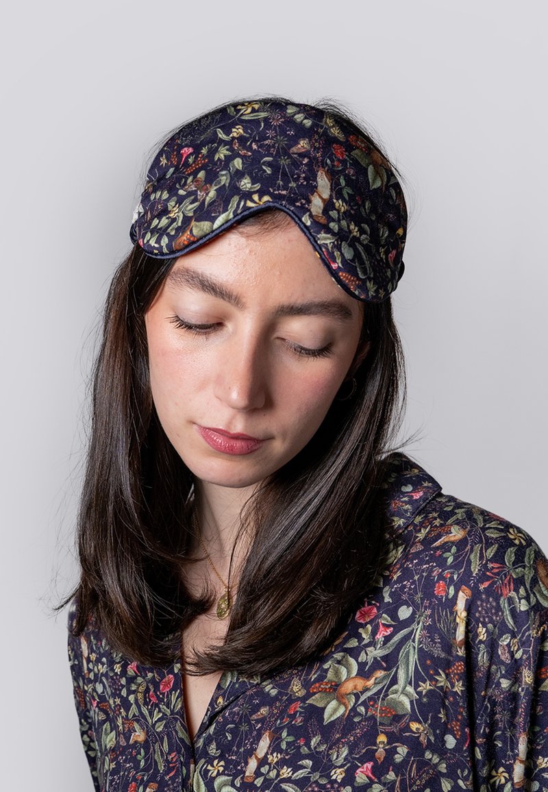 Floral-patterned sleep mask made of soft fabric in dark navy, featuring vivid flowers and woodland creatures, with a contoured design.