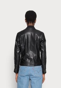Black leather jacket with a fitted design, ribbed shoulders, and side zippers. Features a smooth texture and a subtle sheen.