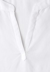 Vêtement en coton blanc avec une encolure en V présentant une patte étroite cousue et de courts petits cols.