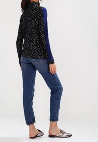 Top negro de manga larga con estampado de leopardo gris, acentos azules en las mangas, combinado con jeans cortos azul claro y zapatos metálicos tipo slide.