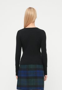 Top negro de manga larga con textura acanalada y escote redondeado, combinado con una falda de cuadros azul y verde, mostrando texturas contrastantes.