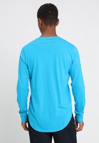 Long-sleeve shirt in bright blue, made of cotton. Features a rounded hem and a classic fit. Smooth texture with stitch detailing on sleeves.