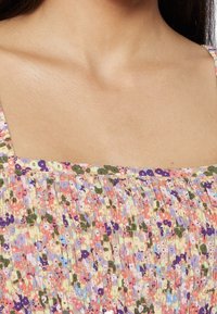 Robe fleurie avec un décolleté carré, smocks texturés dans des tons pastel de rose, vert et violet avec de petits motifs floraux.