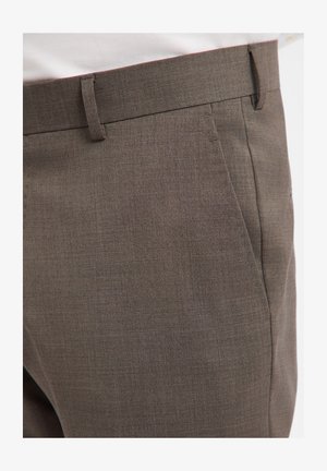 Close-up of brown tailored pants with side pockets and belt loops, worn with a white shirt tucked in.