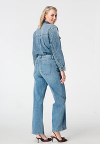 Lichtblauwe spijkerjas en hooggetailleerde jeans met een losse pasvorm. Voorzien van zichtbare naden, klassieke zakken en een subtiel was-effect.