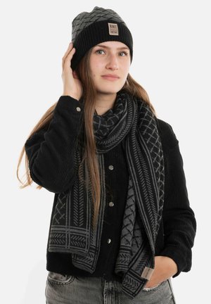 Zwarte gebreide beanie met grijs patroon en logo标签; bijpassende sjaal met zwart en grijs patroon; ribbelstructuur; model draagt een zwart knooptrui.