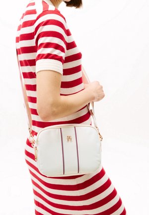 Bolso cruzado blanco con herrajes dorados, que presenta dos franjas verticales en rojo oscuro. El material parece suave y sintético.