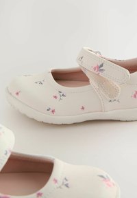 Scarpe chiare con motivi floreali in rosa e viola, dotate di una fascia in Velcro e una punta arrotondata. Materiale morbido e suola bianca.