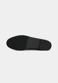 Semelle de chaussure noire avec un design lisse et plat. Présente une zone antidérapante texturée avec une légère courbure au talon. Forme minimaliste et ergonomique.