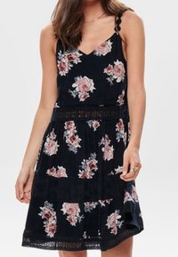 Robe fleurie noire avec un décolleté en V et des bretelles fines, présentant un motif floral en rose et blanc, et des détails en dentelle le long de la taille.