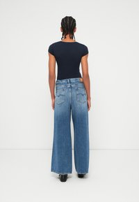 Ναυτικό κοντομάνικο κορμάκι συνδυασμένο με ψηλόμεσα, φαρδιά τζιν που είναι ξεθωριασμένα μπλε, με ακατέργαστο τελείωμα και δύο πίσω τσέπες.