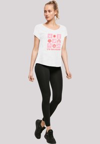 White short-sleeve T-shirt with pink graphic design featuring various icons. Paired with black leggings and black sneakers.