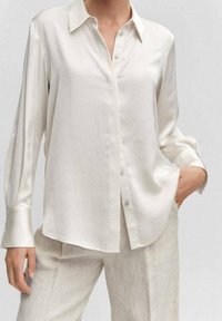 Cream-colored long-sleeve button-up shirt with a collar, lightweight fabric, and a relaxed fit. Features subtle sheen and classic button details.