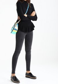 Zwarte peplumtop met lange mouwen, gecombineerd met donkere skinny jeans. Zwarte gepatineerde veterschoenen en een iriserende crossbodytas.