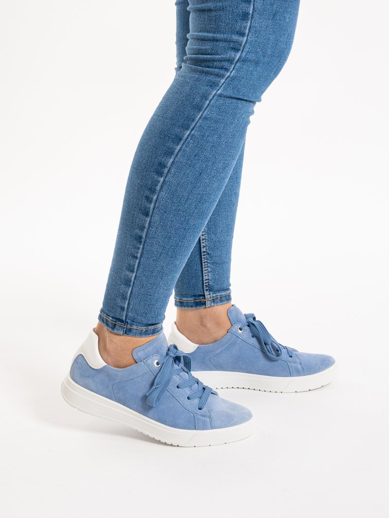 Beine in blauen Skinny-Jeans, die hellblaue Wildledersneaker mit weißen Sohlen und Absätzen tragen, stehen auf weißem Hintergrund.