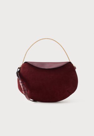 Sac demi-lune en daim bordeaux avec rabat en cuir, bandoulière ajustable et poignée chaîne en or sur un fond clair uni.