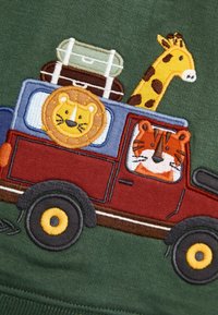 Camion rosso con ruote gialle, decorato con ricami di un leone, una tigre e un giraffa, e bagagli impilati, ambientato su uno sfondo verde.
