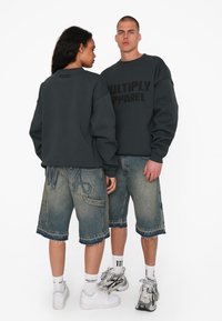 Sweatshirt oversize gris foncé avec "MULTIPLY APPAREL" en noir, associé à un short en denim bleu clair avec des détails de couture visibles.