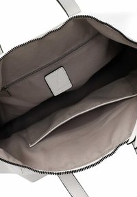 Weiße Leder-Shopper-Tasche mit einem Reißverschluss. Das Innere ist mit grauem Stoff ausgekleidet und verfügt über eine Reißverschlusstasche sowie ein Etikett mit Logo.