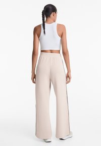 Gekürztes weißes geripptes Tanktop kombiniert mit beigen weiten Sweatpants, die seitliche Streifen und einen elastischen Bund haben. Glatte Stofftextur.