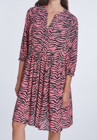 Robe rose avec motif rayures de tigre noires, encolure en V, manches trois-quarts et taille froncée, avec un tissu fluide et texturé.