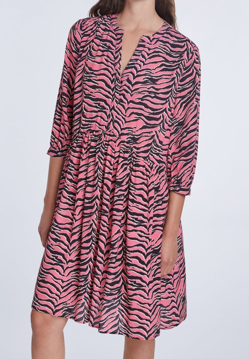 Robe rose avec motif rayures de tigre noires, encolure en V, manches trois-quarts et taille froncée, avec un tissu fluide et texturé.