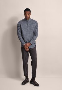 Helles Blaues Langarmhemd mit kleinen weißen Punkten, Knopfleiste vorne, kombiniert mit dunkelgrauen maßgeschneiderten Hosen und braunen Lederschuhen.